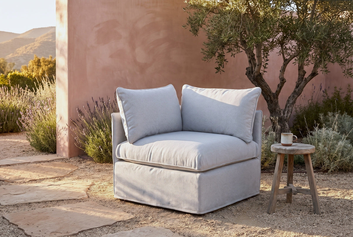 Lentini slipcovered corner chair in light grey in an Ojai hillside garden at golden hour, a terracotta-pink plaster wall and an olive tree behind (stool not included)