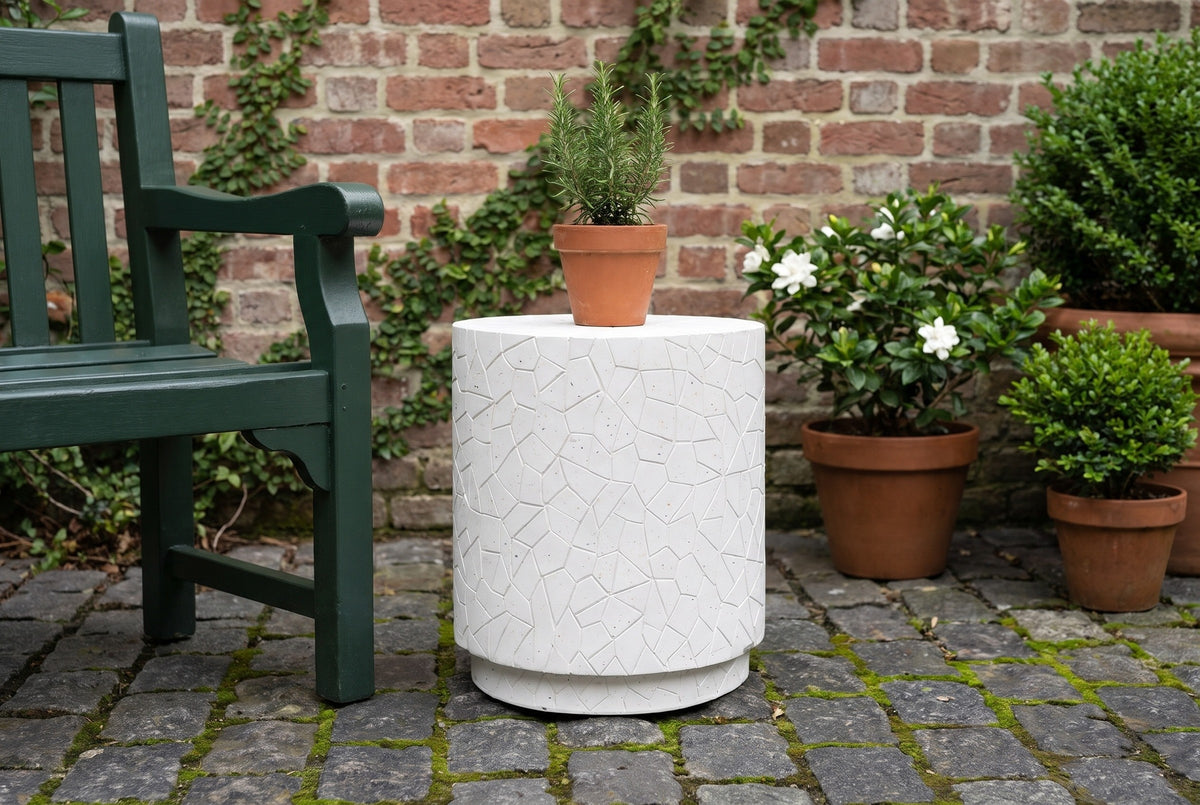 Linguaglossa white concrete drum side table on mossy granite cobbles in a Charleston walled garden, an old brick wall, gardenias and a green garden bench beside it (bench and plants not included)