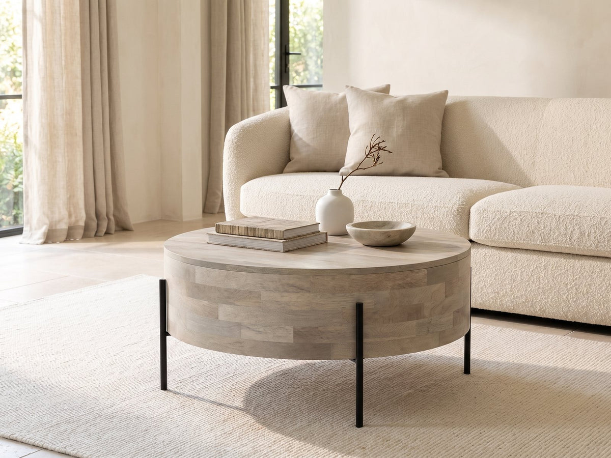Lucignano Whitewashed Mango Drum Coffee Table styled with books, a vase and a stone bowl in front of a cream sofa in a bright plaster room