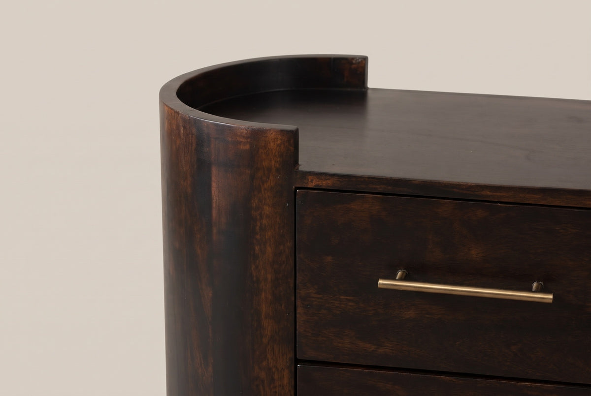 One end of the Macomer nightstand: the half-round mango column with its low curved rim above the flat top, beside the two drawers with slim brass bar pulls
