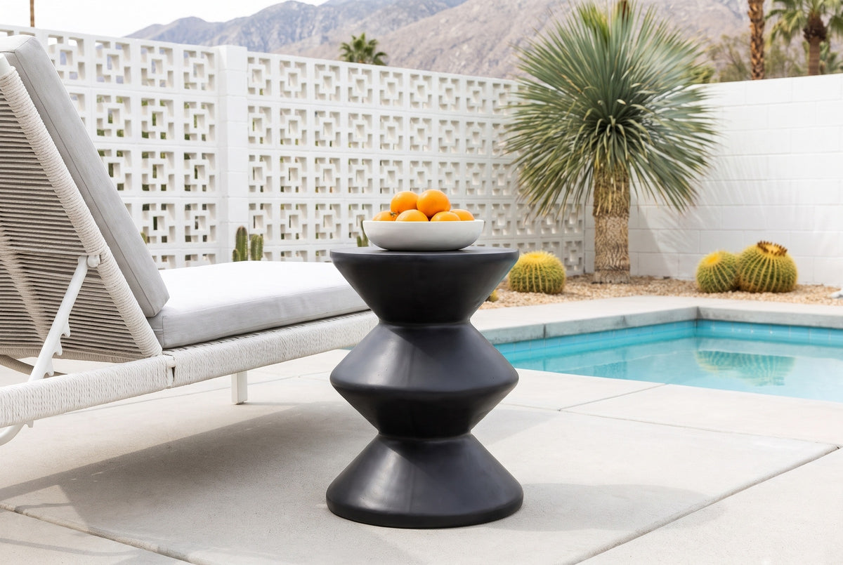Marineo black concrete zigzag side table with a bowl of oranges beside a white rope chaise on a Palm Springs pool patio, a white breeze-block wall, barrel cacti and mountains behind (chaise and decor not included)