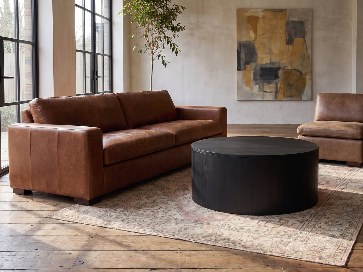 Marostica Black Mango Drum Coffee Table seen from the side, on a vintage rug in front of a leather sofa in an industrial loft