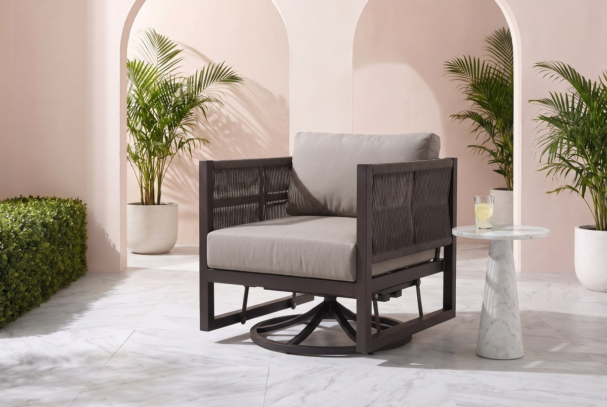 The Marsala swivel glider lounge chair in dark brown with taupe cushions in a Coral Gables courtyard with a blush-pink stucco wall, arched openings, white marble pavers and potted palms (side table not included)