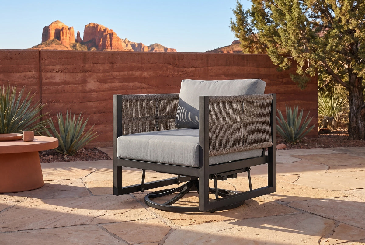 The Marsala swivel glider lounge chair on a sandstone patio in Sedona, Arizona, a rust-red rammed-earth wall, desert plants and the red rock buttes behind (side table not included)