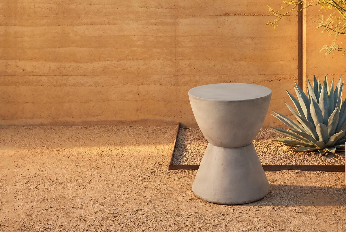 Mazzaro light grey concrete hourglass side table on a gravel patio in Scottsdale, an ochre rammed-earth wall, an agave and a lounge chair behind (chair not included)