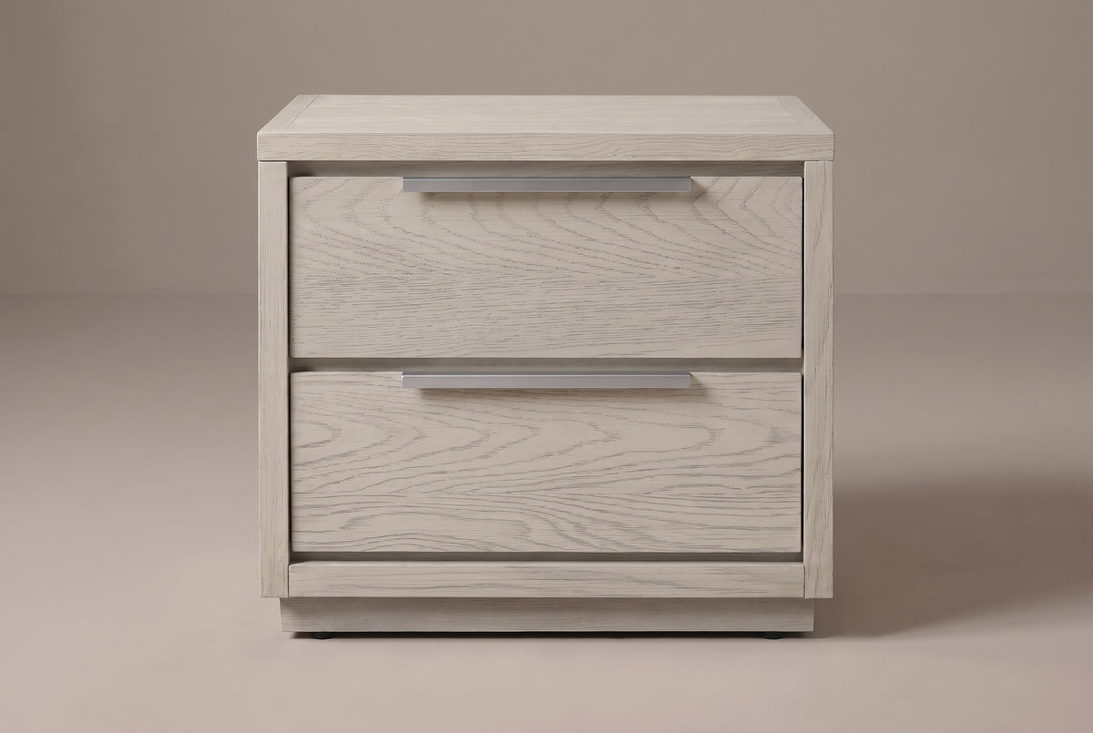 The Melfi nightstand in wire-brushed gray oak, front view on a warm studio backdrop: two stacked drawers with long brushed metal pulls above a low plinth