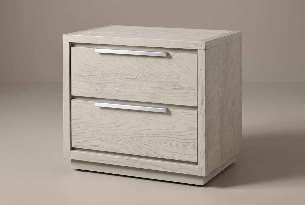 The Melfi two-drawer nightstand in wire-brushed gray oak with long brushed metal edge pulls and a low plinth, three-quarter view on a warm studio backdrop