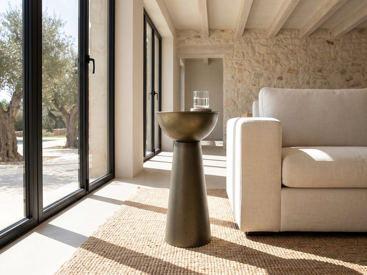 Melpignano Antique Gold Iron Pedestal Side Table beside a linen sofa in a poolside villa