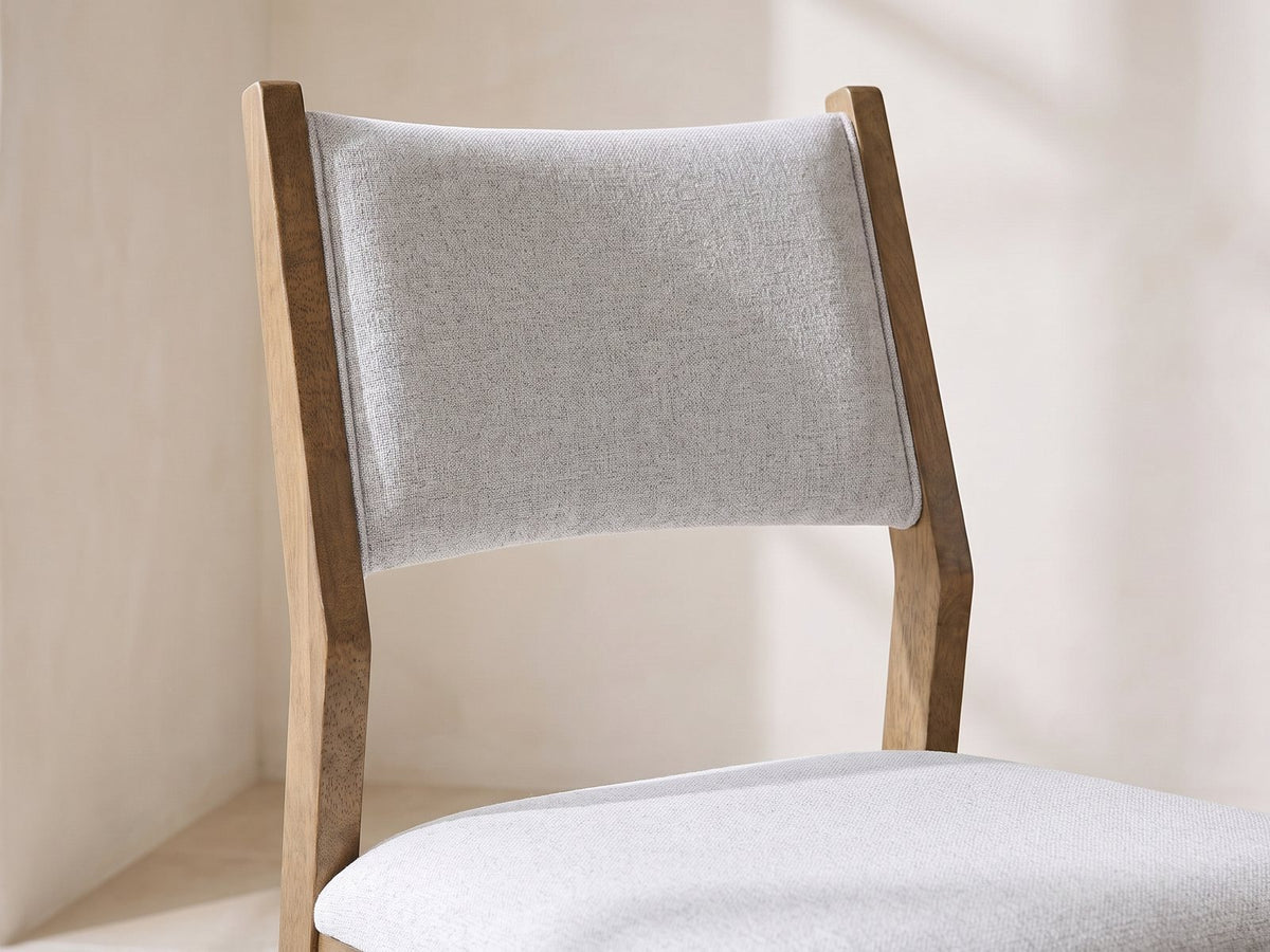 Close-up of the Mileto 72-Inch Light Oak Trestle Dining Set with 6 Upholstered Chairs: the curved upholstered back of a chair between light oak posts