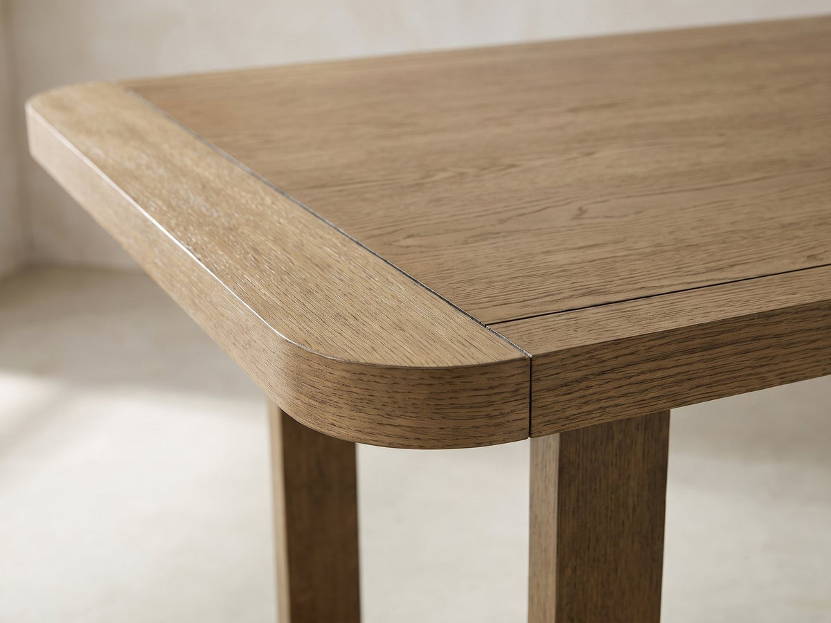 Close-up of the Mileto 72-Inch Light Oak Trestle Dining Set with 6 Upholstered Chairs: a rounded breadboard corner of the light oak top over one post of the trestle base
