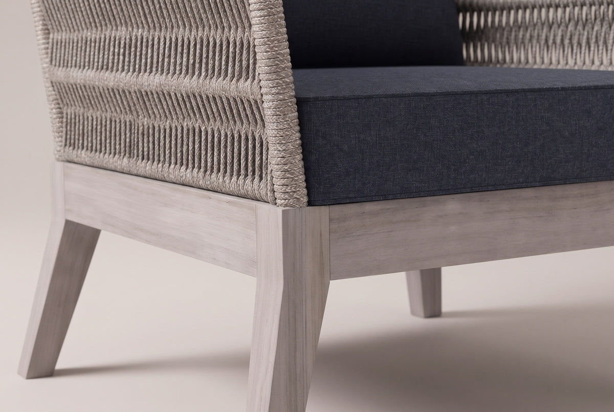 Close view of a Mistretta front corner: the greywash acacia base rail, a splayed square leg, the rope-wrapped arm and the slate grey seat cushion