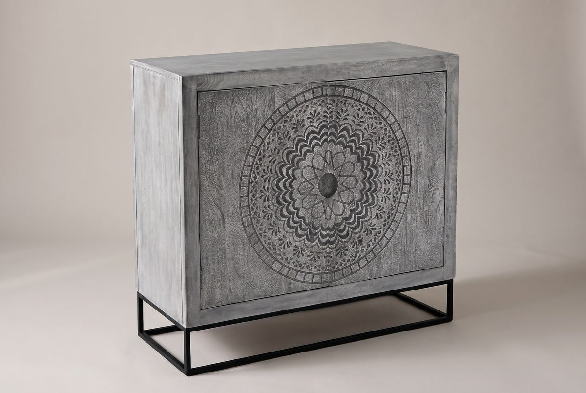 The Molfetta accent cabinet in sandblasted grey mango wood with a round carved medallion across both doors, three-quarter view on a light studio backdrop