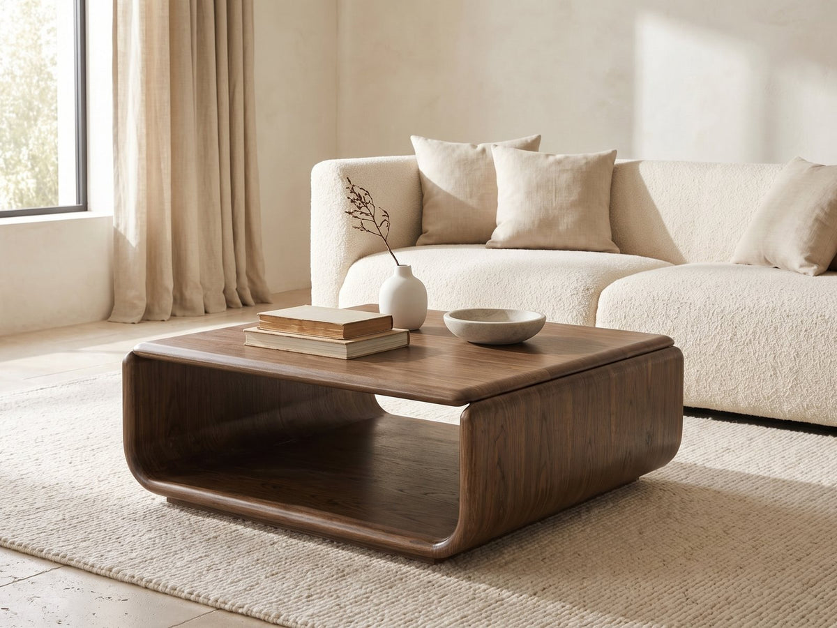 Molveno Walnut-Tone Wood Veneer Coffee Table styled with books, a vase and a stone bowl in front of a cream sofa in a bright plaster room