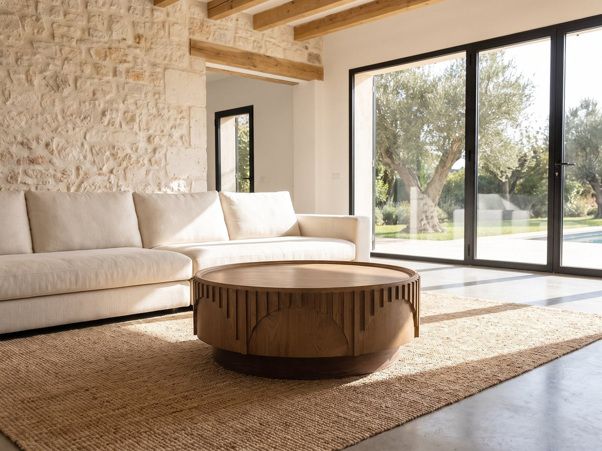 Mondovi 36-Inch Round Carved Limed Ash Drum Coffee Table on a jute rug in front of a linen sofa in a poolside villa
