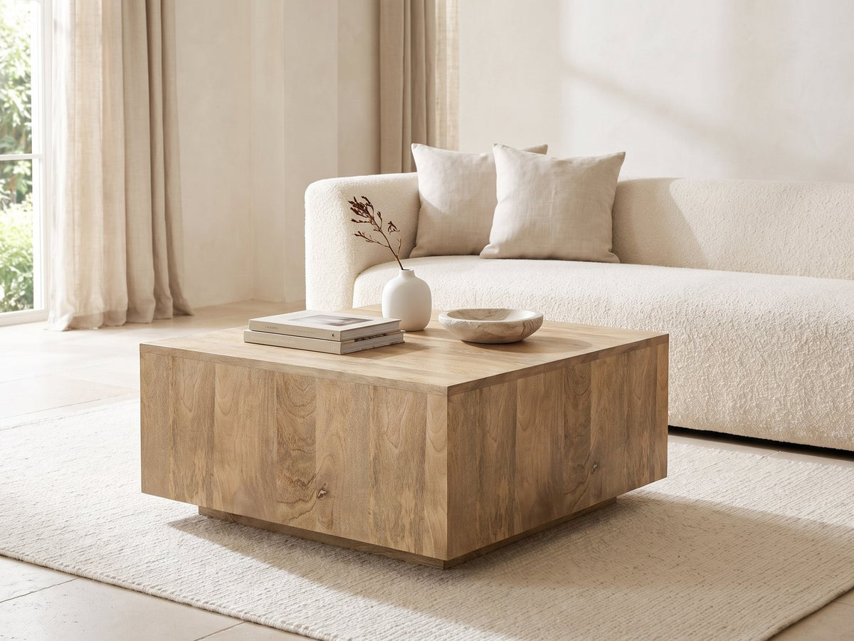Montecatini Square Mango Coffee Table styled with books, a vase and a stone bowl in front of a cream sofa in a bright plaster room