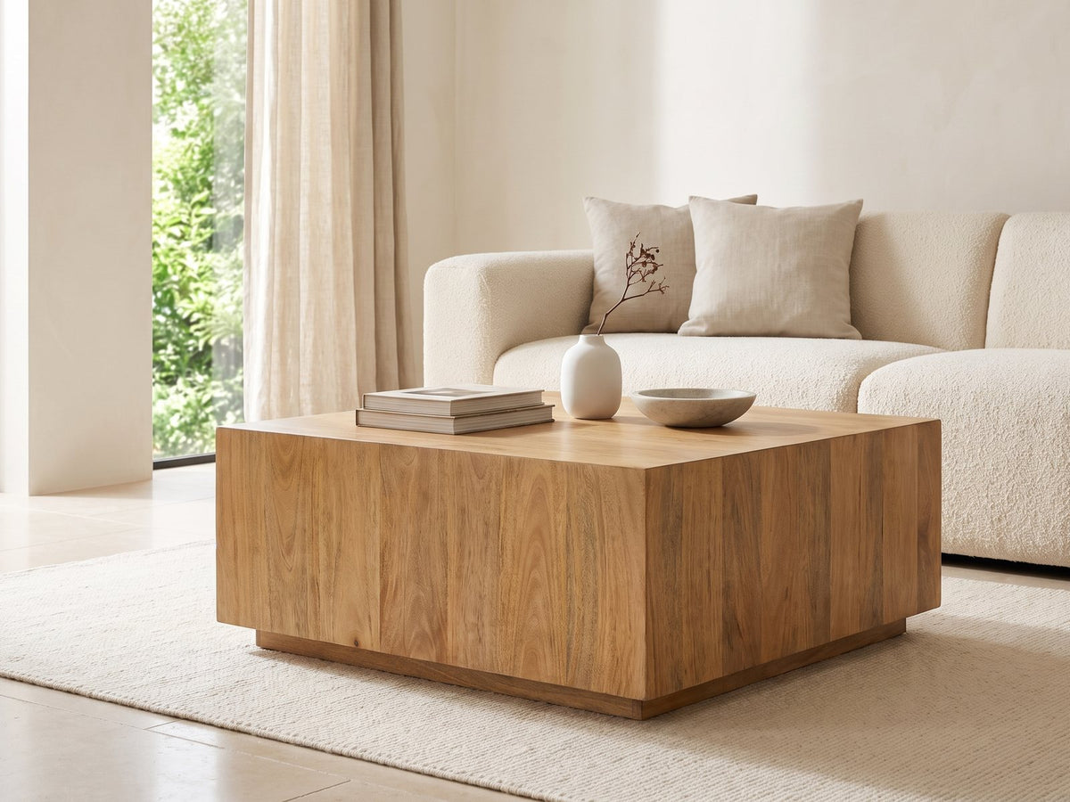 Montecatini Square Mango Coffee Table seen from the side, styled with books, a vase and a stone bowl in front of a cream sofa in a bright plaster room