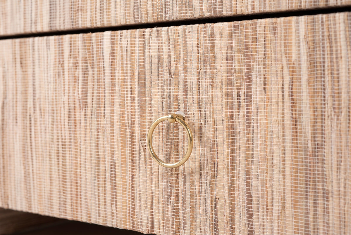 The drawer front of the Muravera nightstand with its gold-tone ring pull, the grass strands running straight up and down around it