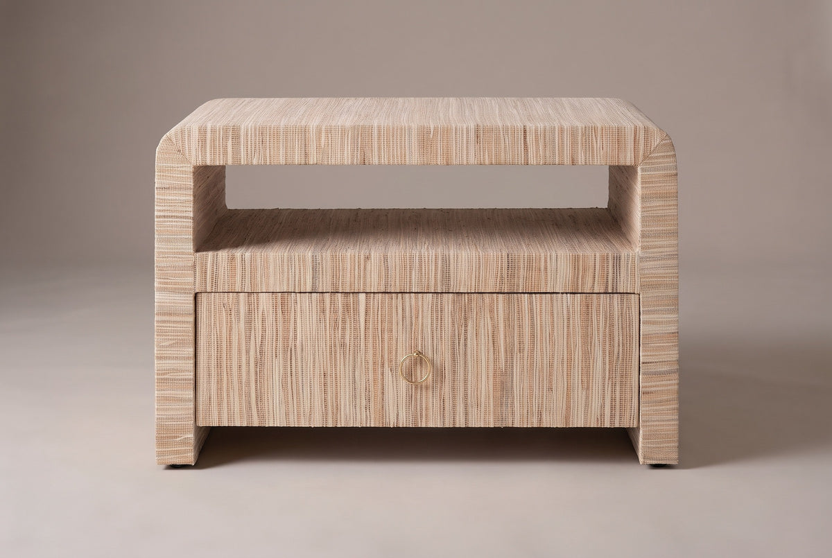 The Muravera nightstand wrapped in natural grasscloth, front view on a light studio backdrop: rounded top corners, open shelf, one drawer with a ring pull and two side panels
