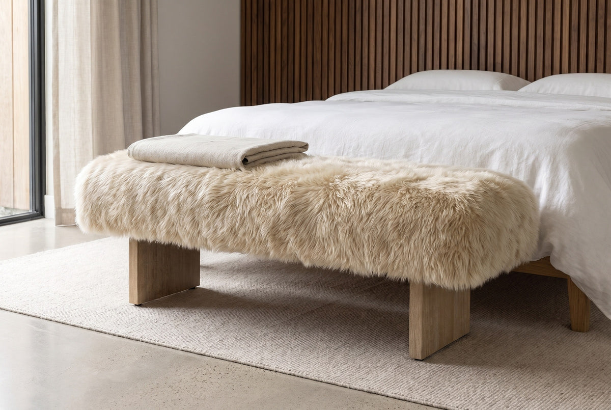 Narni sheepskin bench with a folded linen blanket at the foot of a white-linen bed in a Los Angeles bedroom with a walnut slat wall and a pale concrete floor
