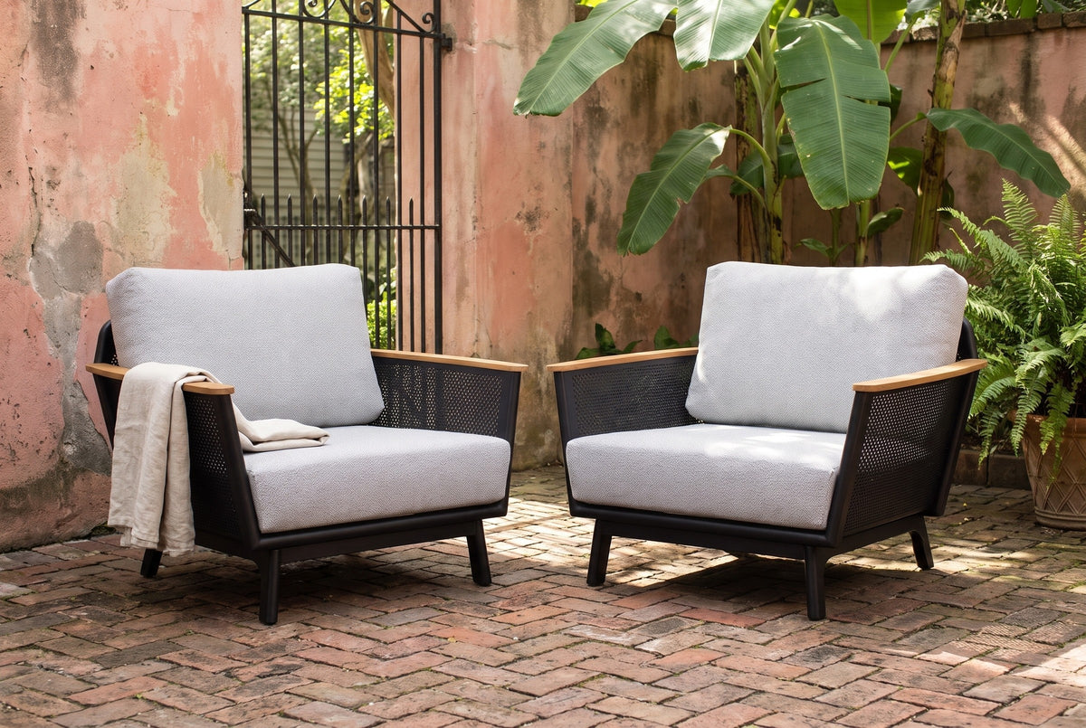 Two Naxos accent chairs on old herringbone brick in a New Orleans courtyard, a faded pink plaster wall and banana leaves behind (throw not included)