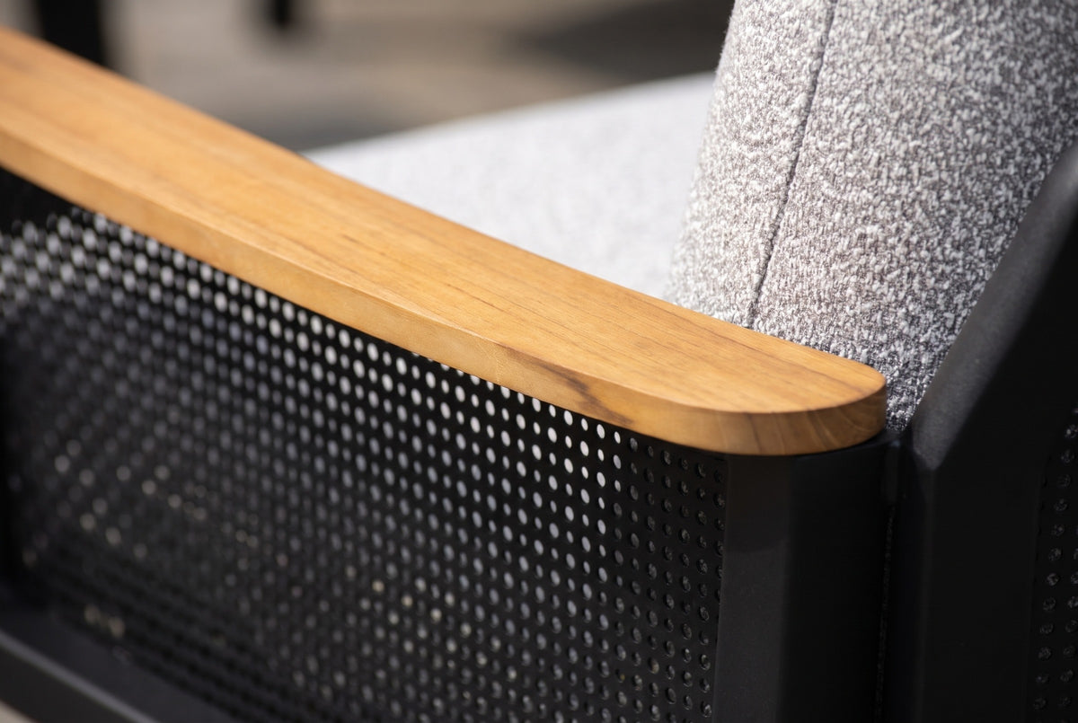 Close-up of a Naxos arm: the solid teak armrest over the black perforated aluminum side panel, beside a light grey textured back cushion