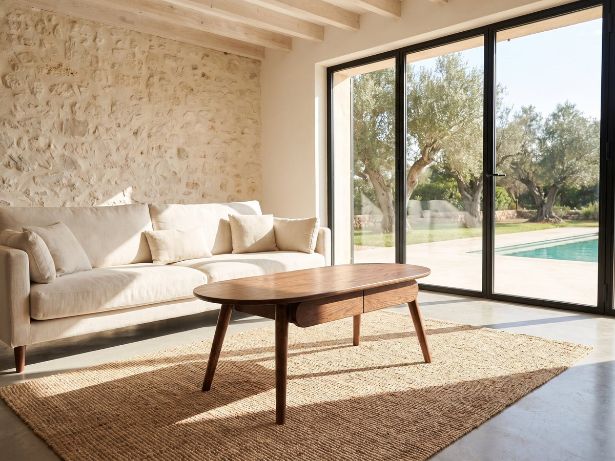 Neive 47-Inch Oval Walnut-Stained Solid Oak Coffee Table with 2 Drawers on a jute rug in front of a linen sofa in a poolside villa