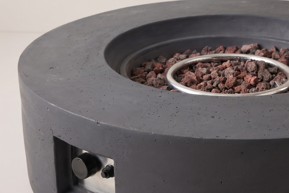 Close-up of the Noto fire pit: the flat dark gray concrete rim, the stepped edge of the centre bowl, lava rocks and the ring burner