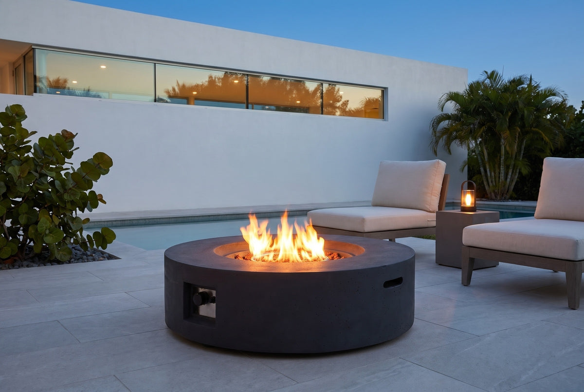 Noto fire pit lit on a pool terrace in Sarasota, Florida at blue hour, a white stucco wall with a band of glass and palms behind (chairs, side table and lantern not included)