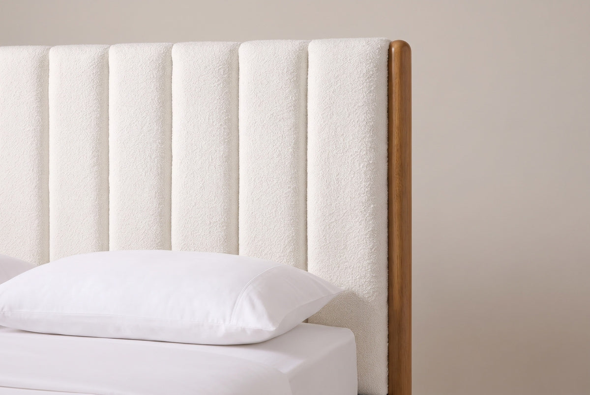 One side of the Ofena headboard: a slim round honey-finish post beside the plump white boucle channels, above a white pillow