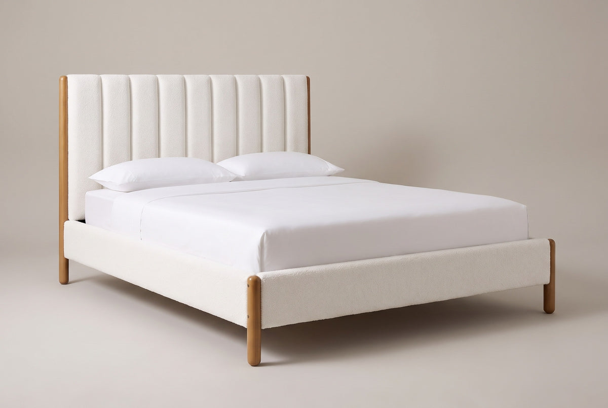 The Ofena white boucle channel bed with honey-finish rubberwood posts, a white mattress and pillows (not included), three-quarter view on a light studio backdrop, Queen shown