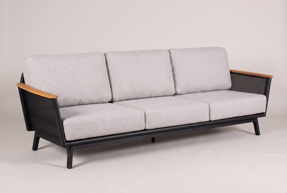 The Ognina outdoor sofa in black aluminum with teak armrests and light grey cushions, three-quarter view on a light studio backdrop