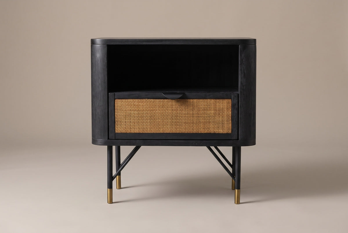 The Olbia nightstand in black acacia, front view on a light studio backdrop: an open niche above one cane drawer, on four slim black legs with brass caps