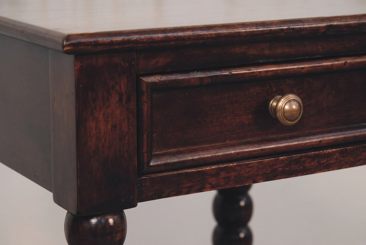 The drawer of the Orani nightstand up close: a flat front in a raised moulding with a round antique brass knob, beneath the softly rounded top
