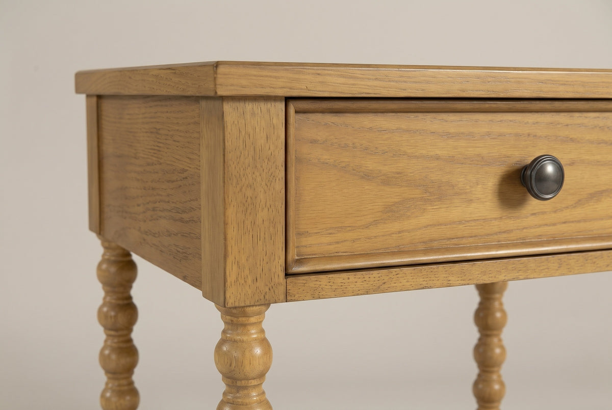 The drawer of the Orgosolo nightstand up close: an oak veneer front with a slim raised lip and a round dark bronze knob, beneath the thin top