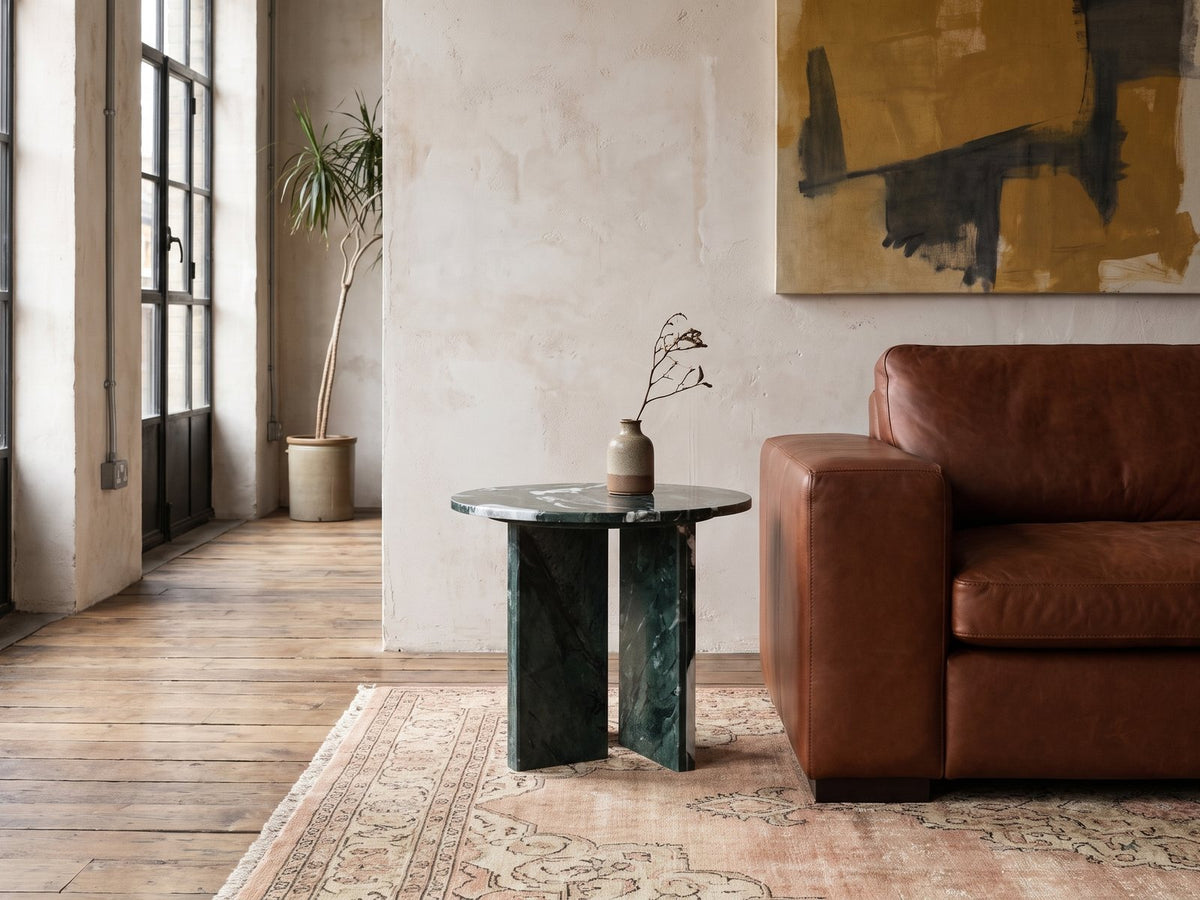 Orosei Verde Marble Round Side Table beside a leather sofa in an industrial loft