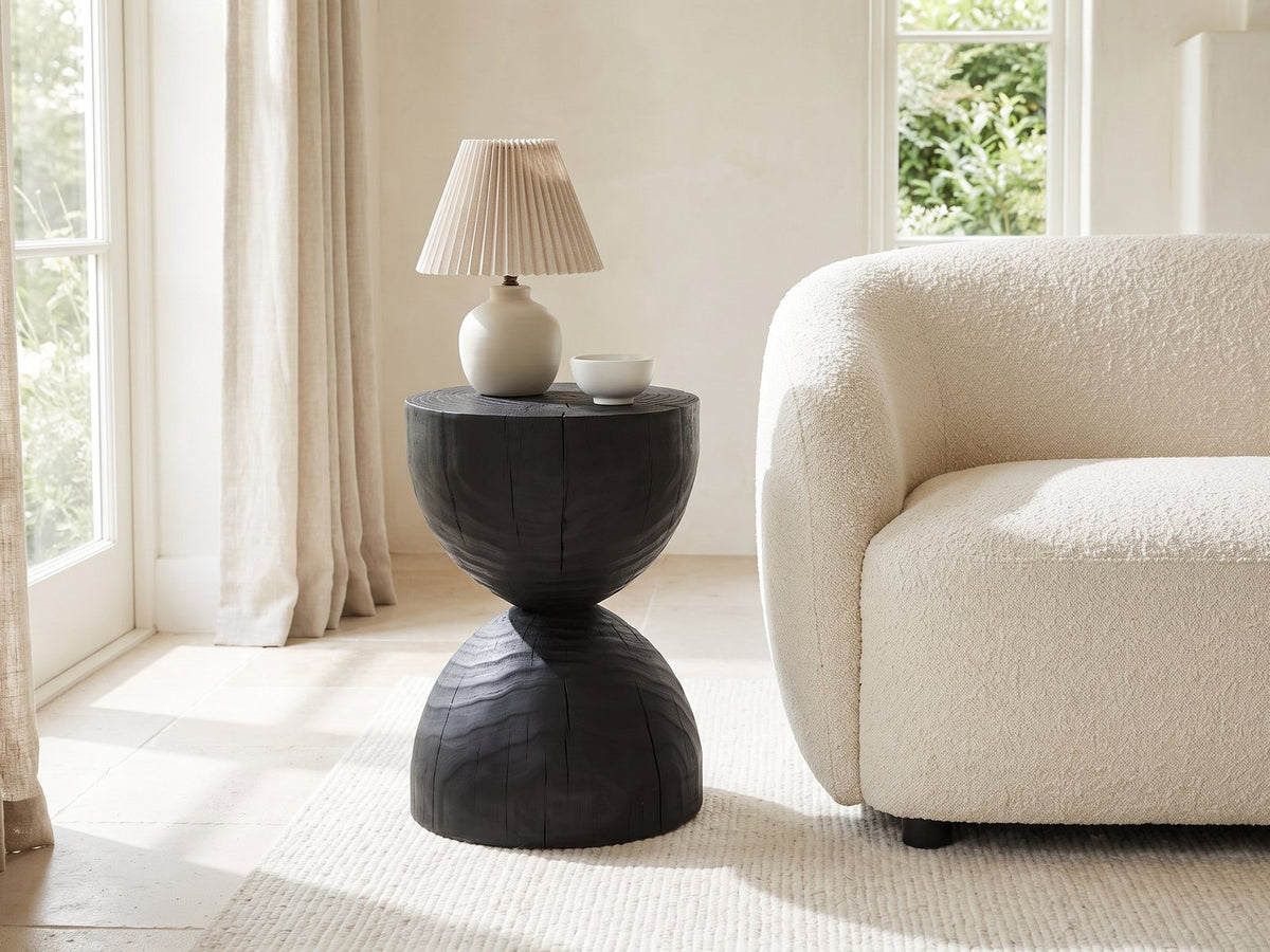 Orta Burnt Mango Hourglass Side Table with a lamp and a ceramic bowl beside a cream boucle armchair in a bright plaster room