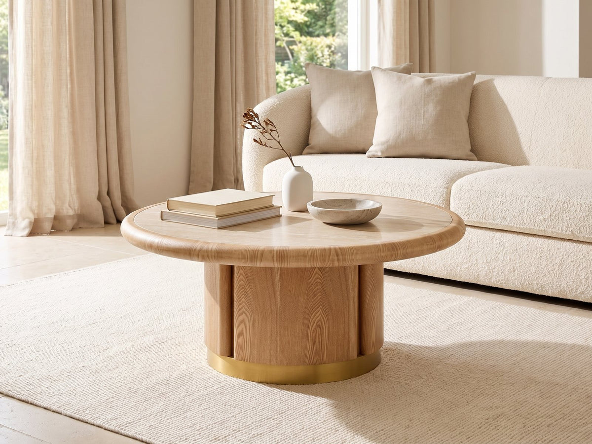 Ovada 35-Inch Round Sintered Stone and Wood Veneer Coffee Table styled with books, a vase and a stone bowl in front of a cream sofa in a bright plaster room