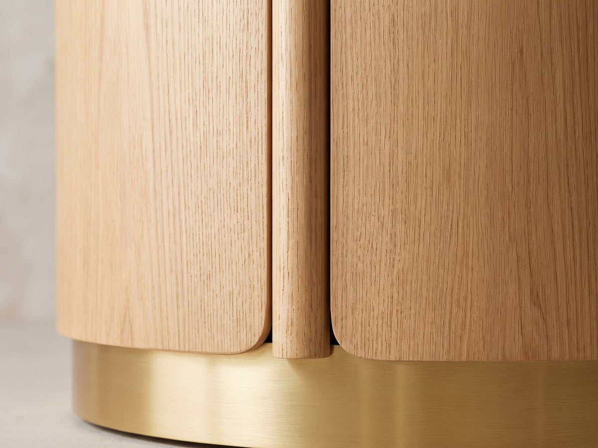 Close-up of the Ovada 35-Inch Round Sintered Stone and Wood Veneer Coffee Table: a rounded wood rail of the drum base meeting the brushed gold band