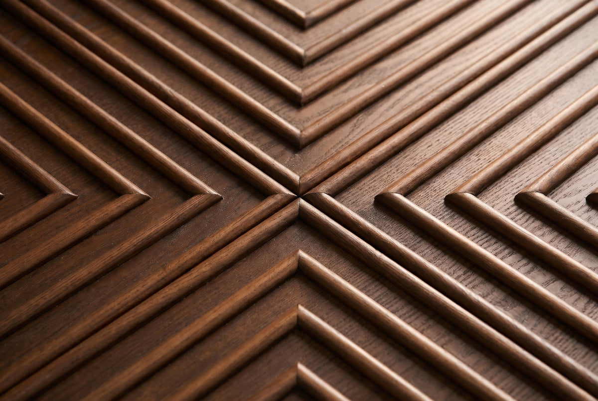 Close-up of the carved relief on the Ozieri nightstand door: raised rounded ash mouldings in nested right angles meeting in a cross, on a darker ground with open ash grain