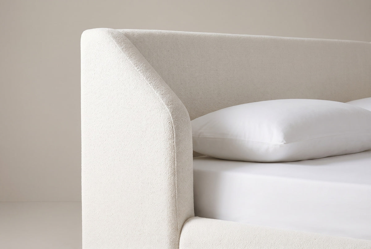 One side of the Pacentro headboard: the white boucle wing with a rounded top corner and a sloping front edge beside the plain flat panel, above a white pillow