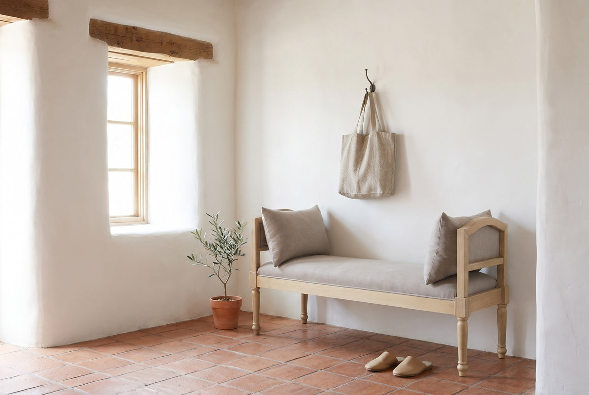 Paciano greige bench against a white lime-washed adobe wall in a Santa Fe entry hall with a terracotta tile floor, an olive tree in a pot and a pair of slippers