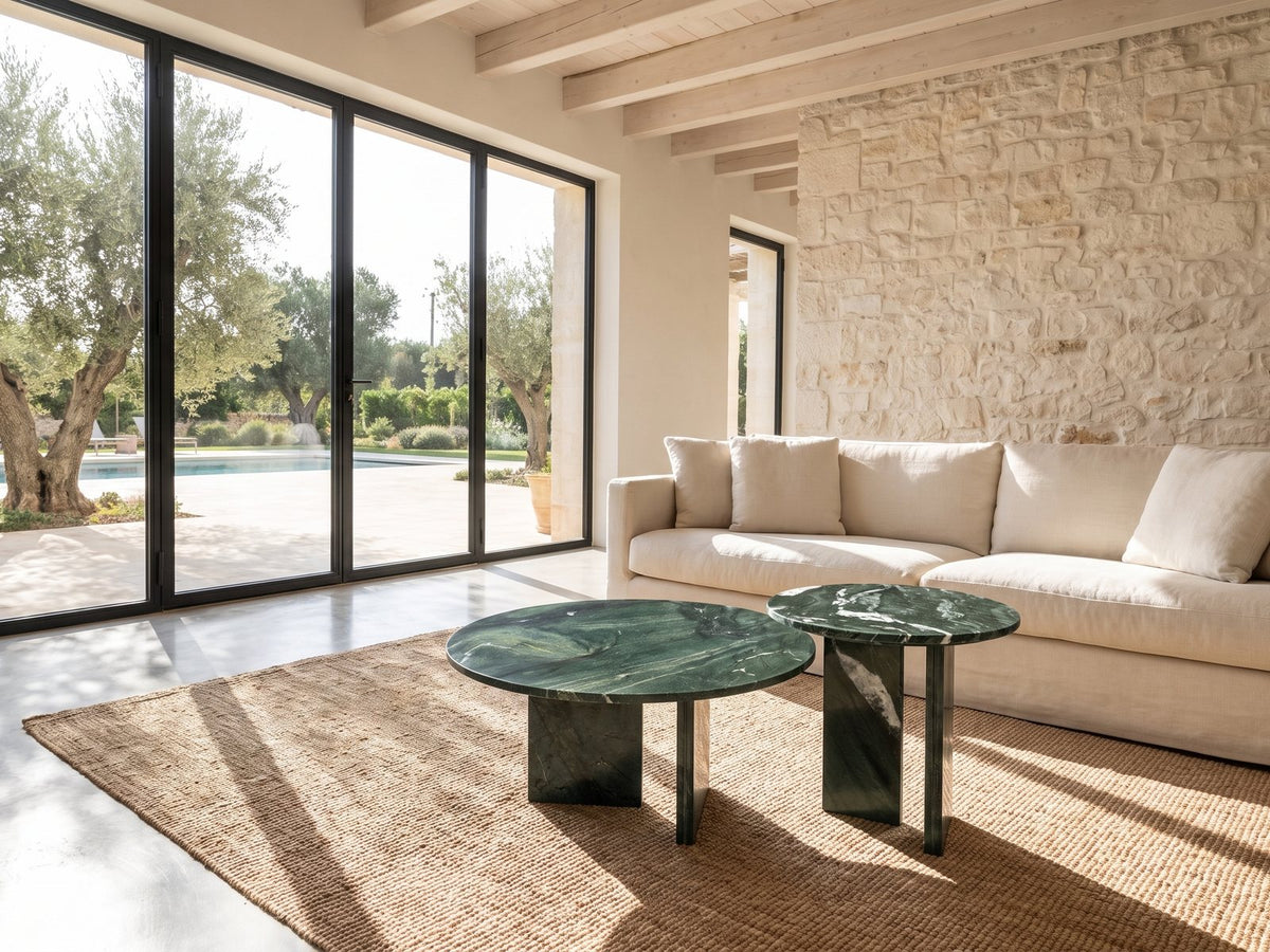 Panarea Verde Marble Nesting Coffee Tables, Set of 2 seen from the side, on a jute rug in front of a linen sofa in a poolside villa