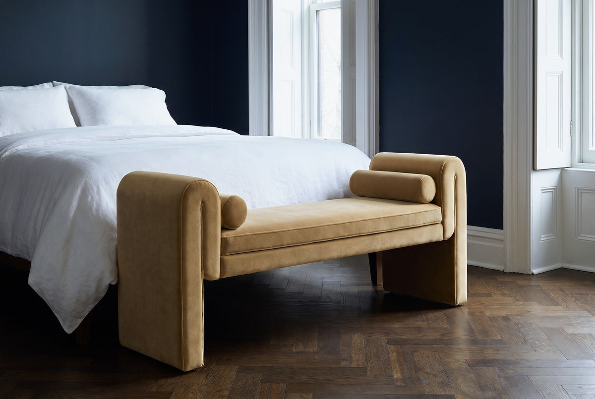Panicale camel velvet bench at the foot of a bed with white linen bedding in a Brooklyn brownstone bedroom with an inky navy wall and a dark herringbone floor (bed not included)