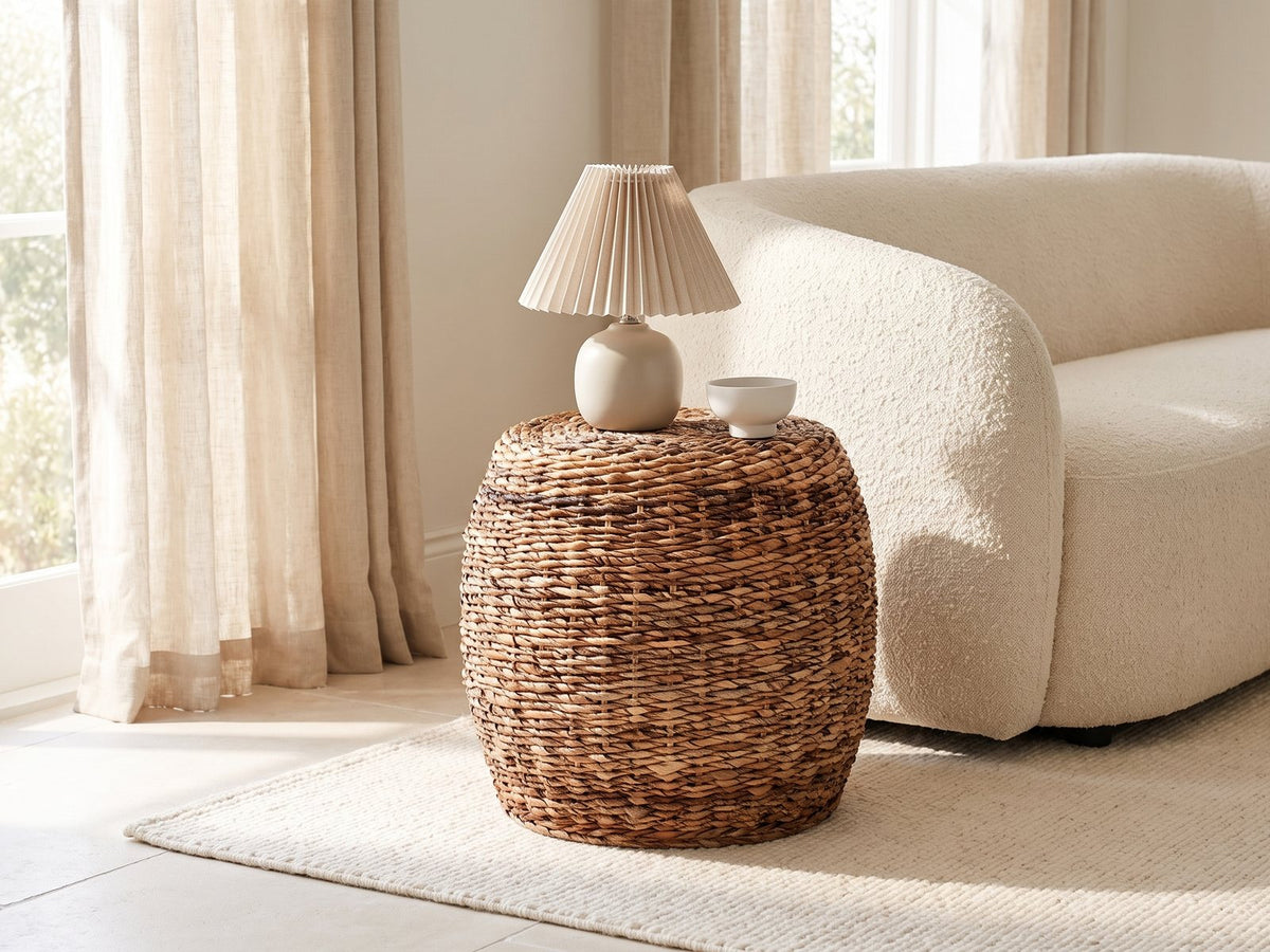 Parabita Woven Natural Fiber Barrel Side Table with a lamp and a ceramic bowl beside a cream boucle sofa in a bright plaster room