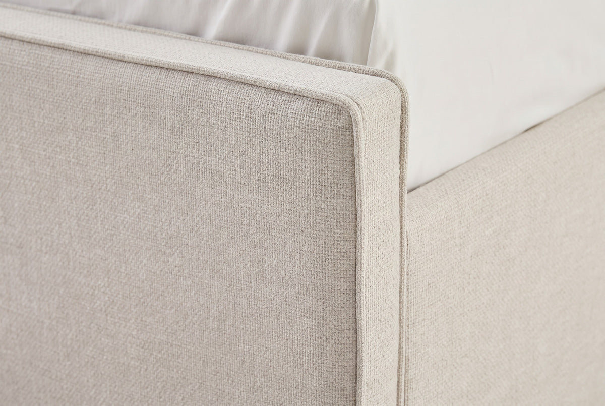 Close-up of the Penne footboard corner in ivory canvas, with the thin self-welt along the top edge and down the corner