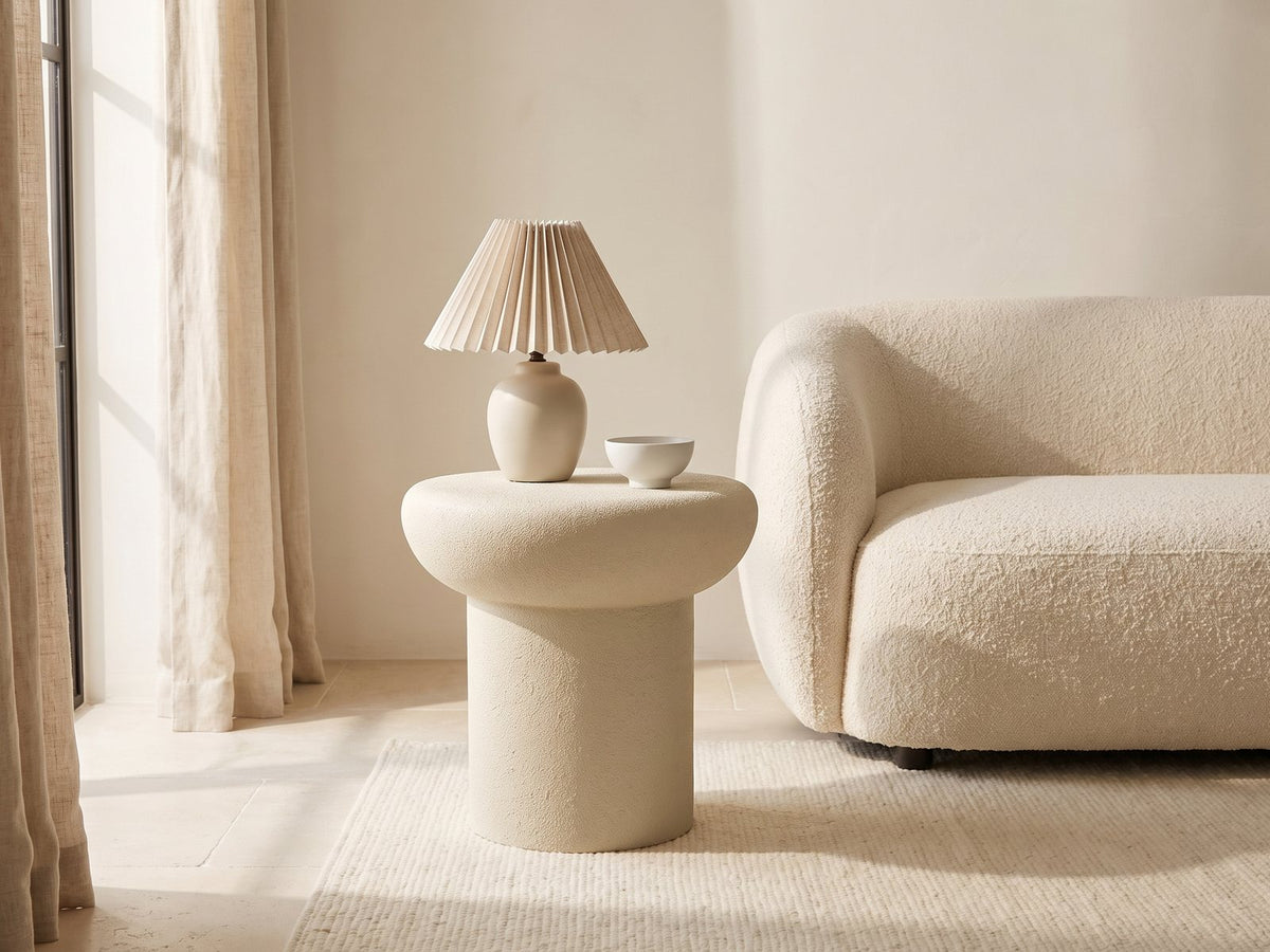 Pescocostanzo Cream Textured Fiberglass Mushroom Side Table with a lamp and a ceramic bowl beside a cream boucle sofa in a bright plaster room