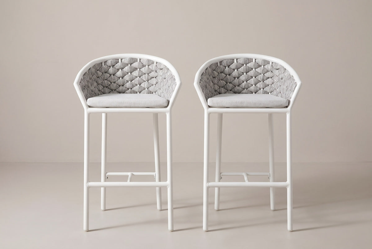 The two Petralia counter stools seen straight from the front: woven barrel backs, pale grey cushions, slim round legs and the footrest rails