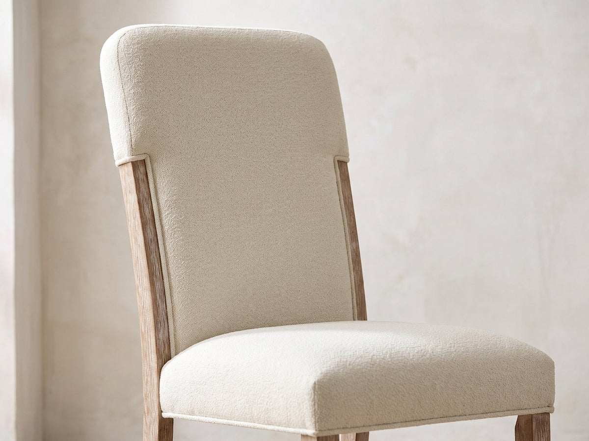 Close-up of the Picinisco 74-Inch Extendable Oak Veneer Dining Set with 4 Chairs: the tall upholstered back, exposed oak posts and padded seat of a chair in beige chenille