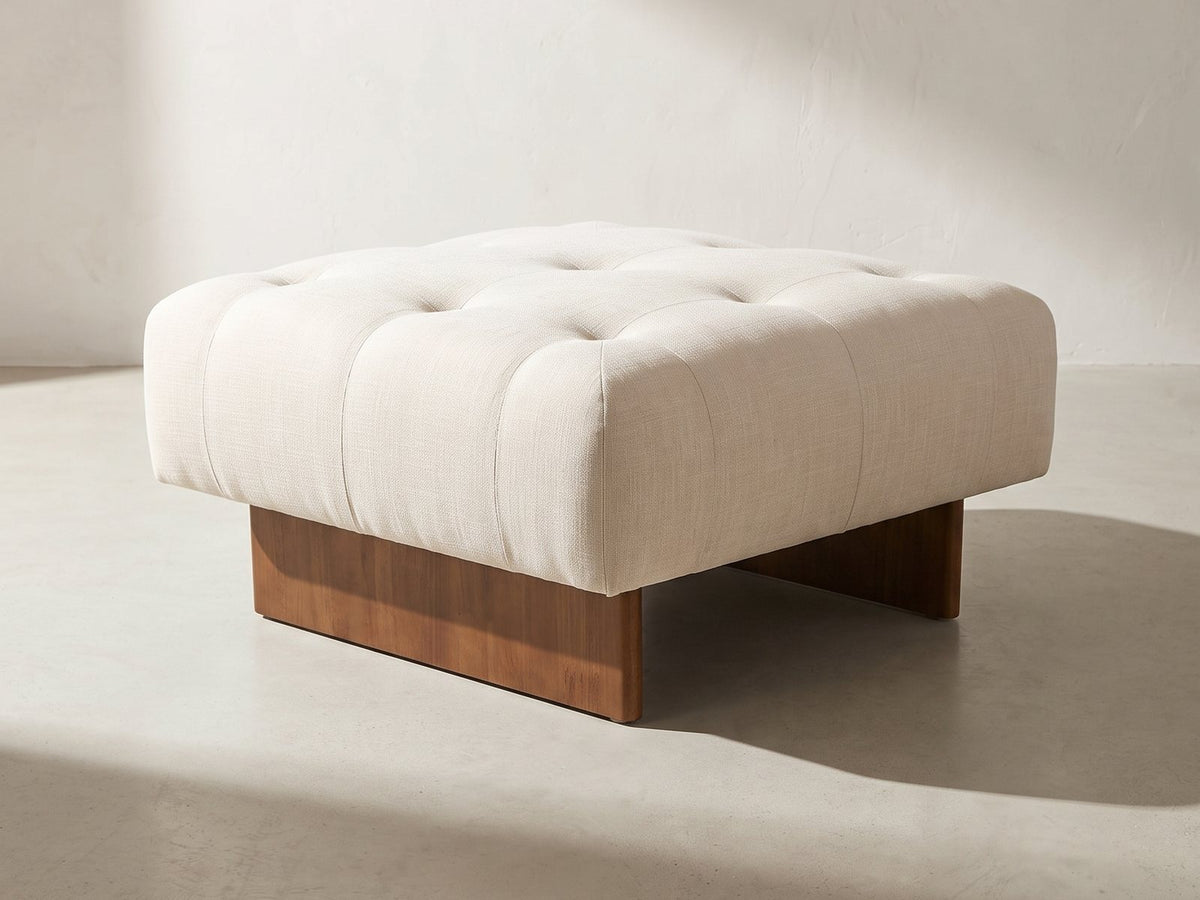 Pienza Tufted Ottoman in ivory against a plaster wall in morning light