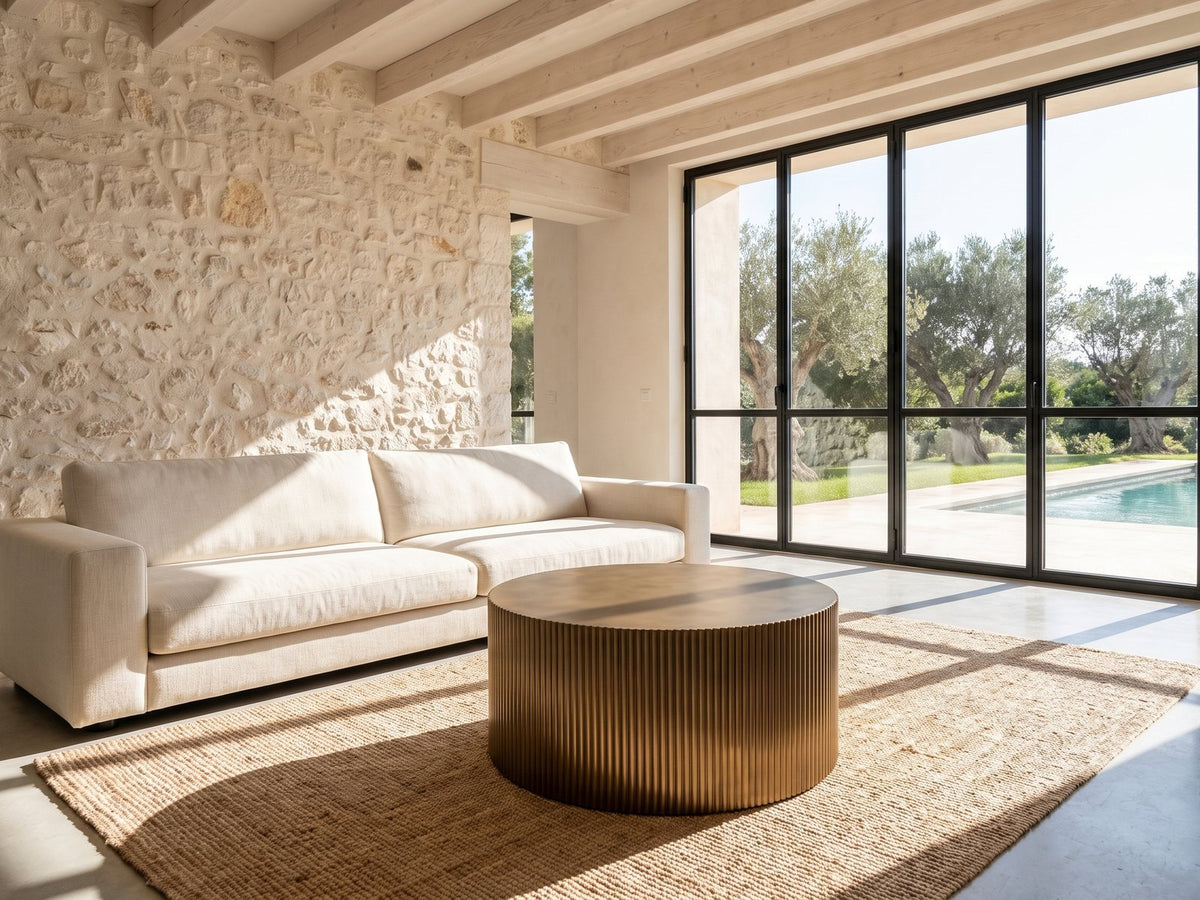 Pitigliano Brass-Finish Fluted Drum Coffee Table on a jute rug in front of a linen sofa in a poolside villa